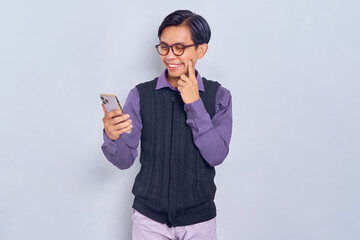 Smiling young Asian man in casual shirt holding mobile phone and thinking about something with finger on chin isolated on white background