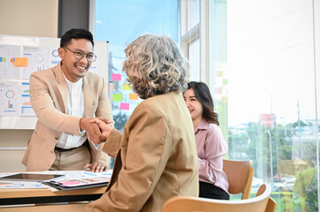 Cheerful Asian businessman shaking hand with senior female executive manager