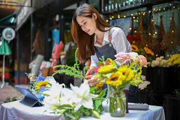 Attractive Asian female florist cutting flower stalk with scissors, arranging flower bouquet.