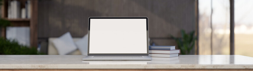 Laptop mockup and books on white marble tabletop over blurred modern loft living room