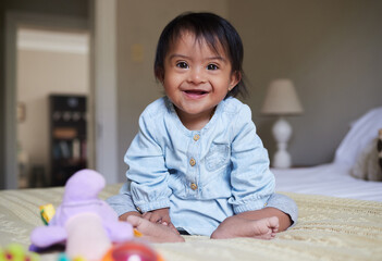 Down syndrome and happy baby portrait on bed with joy of Mexican special needs kid relaxed in home....