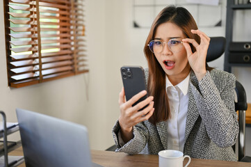 Surprised and shocked sian businesswoman reading an unexpected email on her smartphone