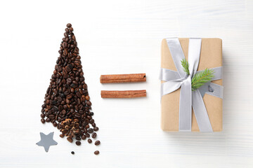 Christmas tree made of coffee beans, star, cinnamon and gift on white wooden background