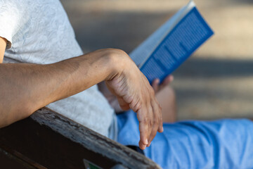 Unrecognizable boy reading a book sitting on a bench.