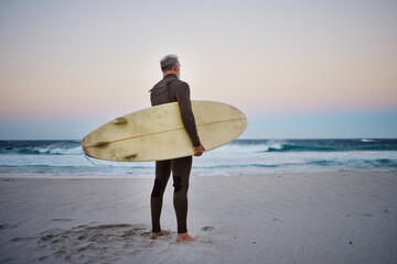 Surfer, surfboard and senior man on beach at sea waves in during sunset during summer vacation in...
