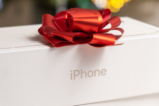 iPhone box with a red bow against a blurred background. Gifts from Apple for Christmas or New Year parties, October 2022, Prague, Czech Republic. 