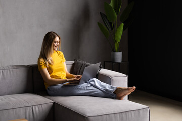 Happy woman using laptop sitting on cosy sofa