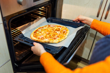 A woman taking out baking tray with delicious pizza from oven on kitchen