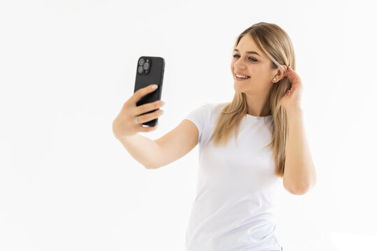 Portrait of a smiling cute woman making selfie photo on smartphone on a white background
