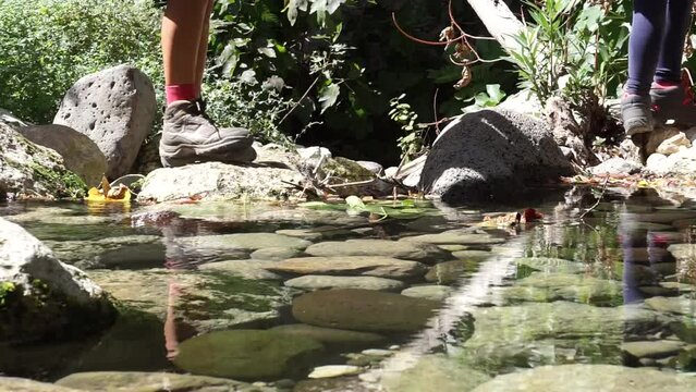 Video del guado di un fiume, dove si vedono le gambe e i piedi degli esploratori che passano da una pietra all'altra
