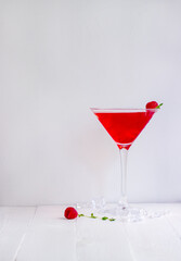 Red alcohol cocktail with raspberries and thyme on the white wood table.