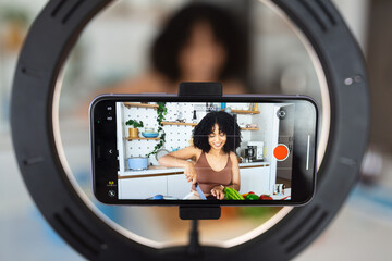 African American woman chef vlogger shoot cooking food vlog blog on smartphone at home kitchen....