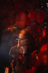 Portrait red-haired woman with closed eyes standing in red autumn trees