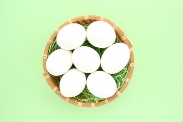 Fresh white chicken eggs in wooden rattan wicker basket on green background. Natural healthy nutrition organic farm food product concept. World egg day, easter holiday composition. Close-up, flatlay