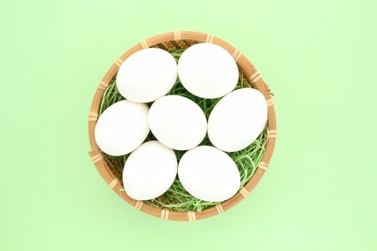 Fresh white chicken eggs in wooden rattan wicker basket on green background. Natural healthy nutrition organic farm food product concept. World egg day, easter holiday composition. Close-up, flatlay