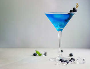 Blue cocktail in martini glass with ice cubes, mint and bluberries