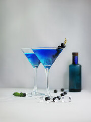 Blue cocktails in martini glass with ice cubes, mint and bluberries and bottle of gin