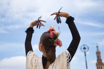 Fototapeta premium Portrait of young teenage girl in black dance dress, white shawl and pink carnations in her hair, dancing flamenco with castanets in her hands. Concept of flamenco, dance, art, typical Spanish dance.