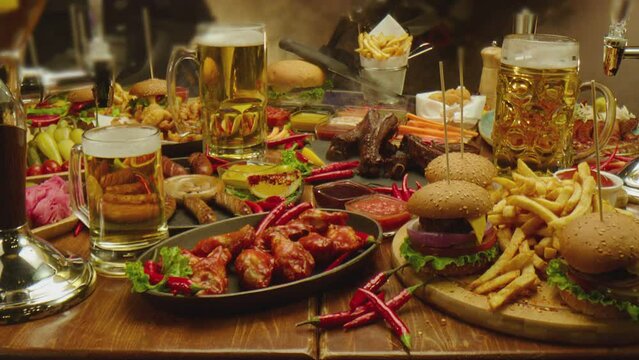 Table served with beer fast food fried fries chicken wings burgers  Austrian sausages various types of sauces . Camera moving across food Shot on ARRI ALEXA Cinema Camera with Laowa lens . Slow motion