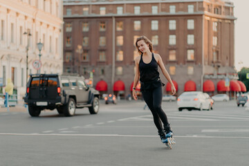Active girl rollerblading on grey asphalt poses on rollers dressed in active wear drives fast leads...