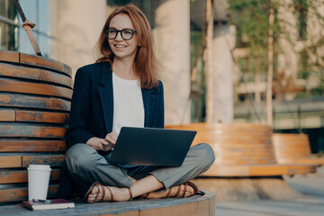 Pleased pretty redhead woman learns educational course on laptop computer