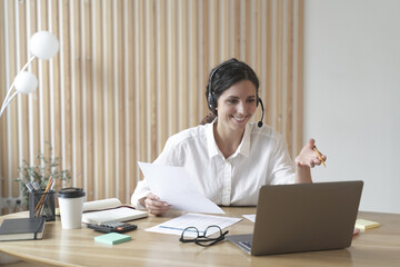 Happy italian female tutor in headset conducts webinar online on laptop in modern home office