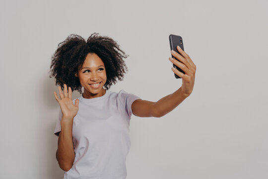 Happy young female waving at camera while having video call with best friend on modern smartphone