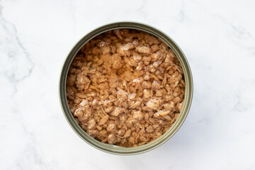Open tin can with chopped tuna in oil on white marble kitchen table. Canned fish in a tin can. Top view, copy space