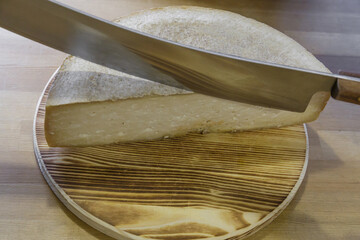 A man cuts a head of cheese with a large knife.
