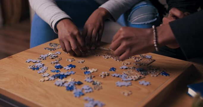 Close-up of the hands of two people of African appearance putting together puzzles. Young people choose the necessary details and try to make picture. They make puzzles on wooden table.