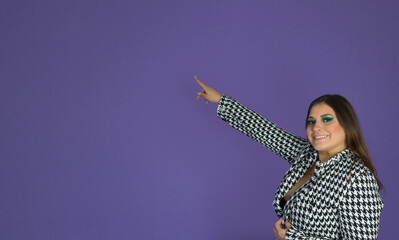 portrait headshot of a pretty woman in makeup pointing up while looking at camera ahead a purple background