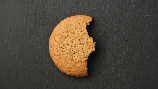 Oatmeal cookie eaten slowly. Disappearing chip cookie on black background. Stop motion of donut cookie bite. Food concept. Top view in 4K, UHD