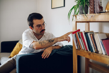 Fashionable hipster man with mustache reading a book while at home.