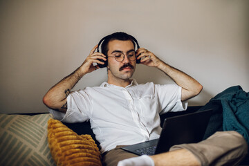 Obraz premium Man with a mustache working on laptop at home and using headphones