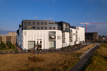 Fototapeta premium White exterior facade of newly build luxury apartment building in Hanseatic city with floodplains in the foreground and construction crane rising above