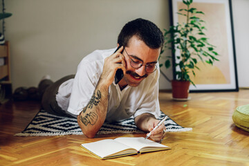 Hipster man using smartphone and taking notes while on the floor at home