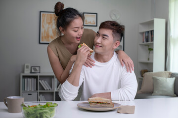 Loving young Asian couple looking at each other while having breakfast. Close up shot of young man and woman having meal at home. Happy young couple eating.