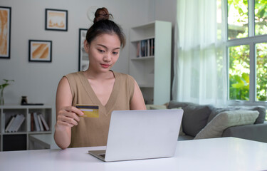 Young Asian woman holding credit card and using laptop computer. Businesswoman working at home. Online shopping, e-commerce, internet banking, spending money, working from home concept