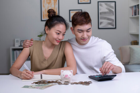 Portrait of a happy Asian couple at home saving money in a piggybank. Happy woman and man couple at home saving money in a piggybank and smiling.