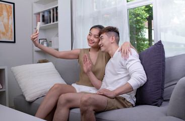 Happy young Asian couple taking selfie on sofa in the living room. Man and Woman couple lifestyle concept.