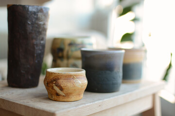 Pottery ceramic products of beige, blue and brown color. Fired and polished. Bowls, cups and vase. Set of handmade ceramic mugs on a wooden table.