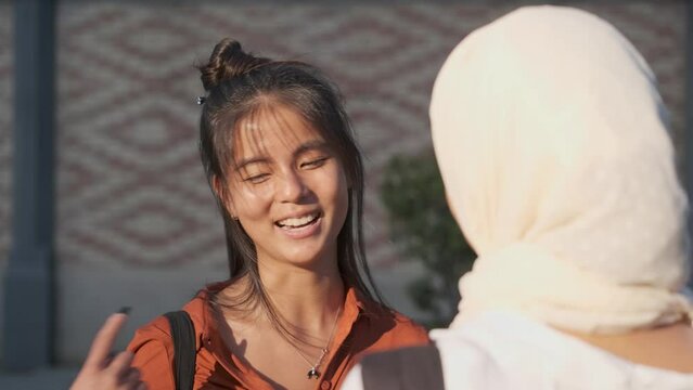 Young Asian woman smiling while chatting with a friend outdoors on the street.