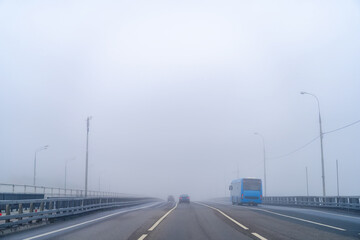 Blue bus and cars are driving along blue empty highway of city road with low visibility on warm...