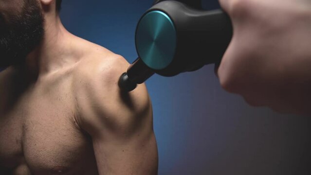 Percussion massage of the shoulder of a male athlete with a shock wave massager. Close-up slow motion. Wave Vibration of the body from the massager.