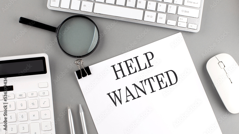 Aufkleber help wanted written on paper with office tools and keyboard on the grey background