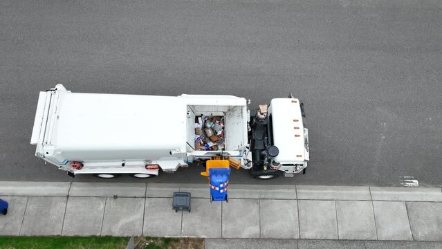Top down drone shot of a dump truck loading a bin of trash with a piece of it falling out.