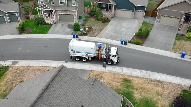 Drone view of a garbage truck loading a bin from the curb of an American neighborhood.