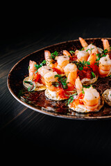 set of Appetizer canape with shrimp, cheese and sauce on a small loaf of bread in plate on black wooden table