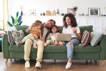 Happy young family is relaxing on the couch with a laptop and books at home
