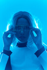 Young woman with futuristic suit and glasses with blue led lights, virtual or metaverse concept, looking at camera